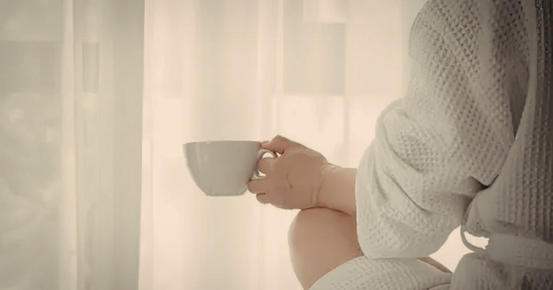 A person seated in soft warm light holding a cup, wearing a knit jumper, representing the quiet stillness of exhaustion that rest does not seem to reach.