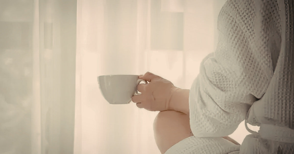 A person seated in soft warm light holding a cup, wearing a knit jumper, representing the quiet stillness of exhaustion that rest does not seem to reach.
